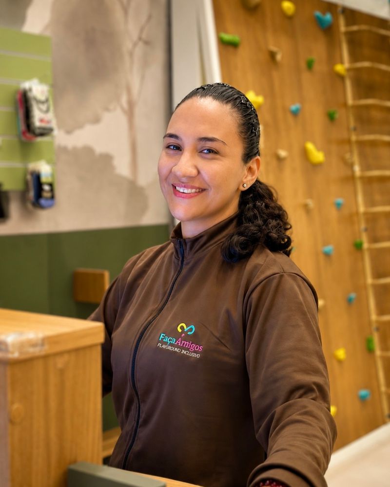 Mediadora do FaçaAmigos sorrindo na recepção, com a parede de escalada ao fundo